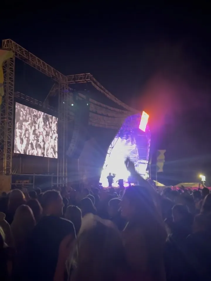 A festival crowd at night facing a bright stage and big screen.